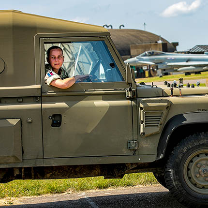 Female RAF Driver driving Land Rover along airfield taxi-way in front of Typhoon jet