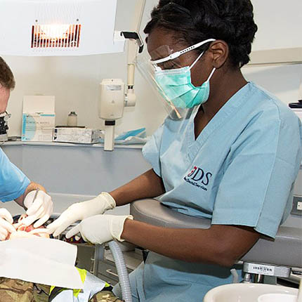 RAF Dental Nurse in mask and faceshield assisting RAF Dentist with patient