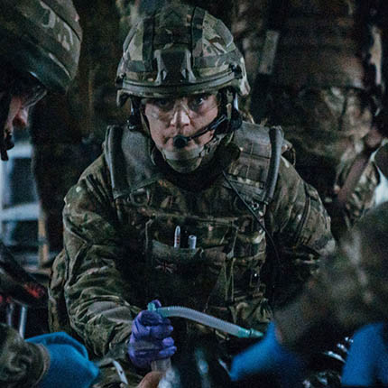 RAF Registered Nurse in full combat clothing assisting with casualty on stretcher inside helicopter