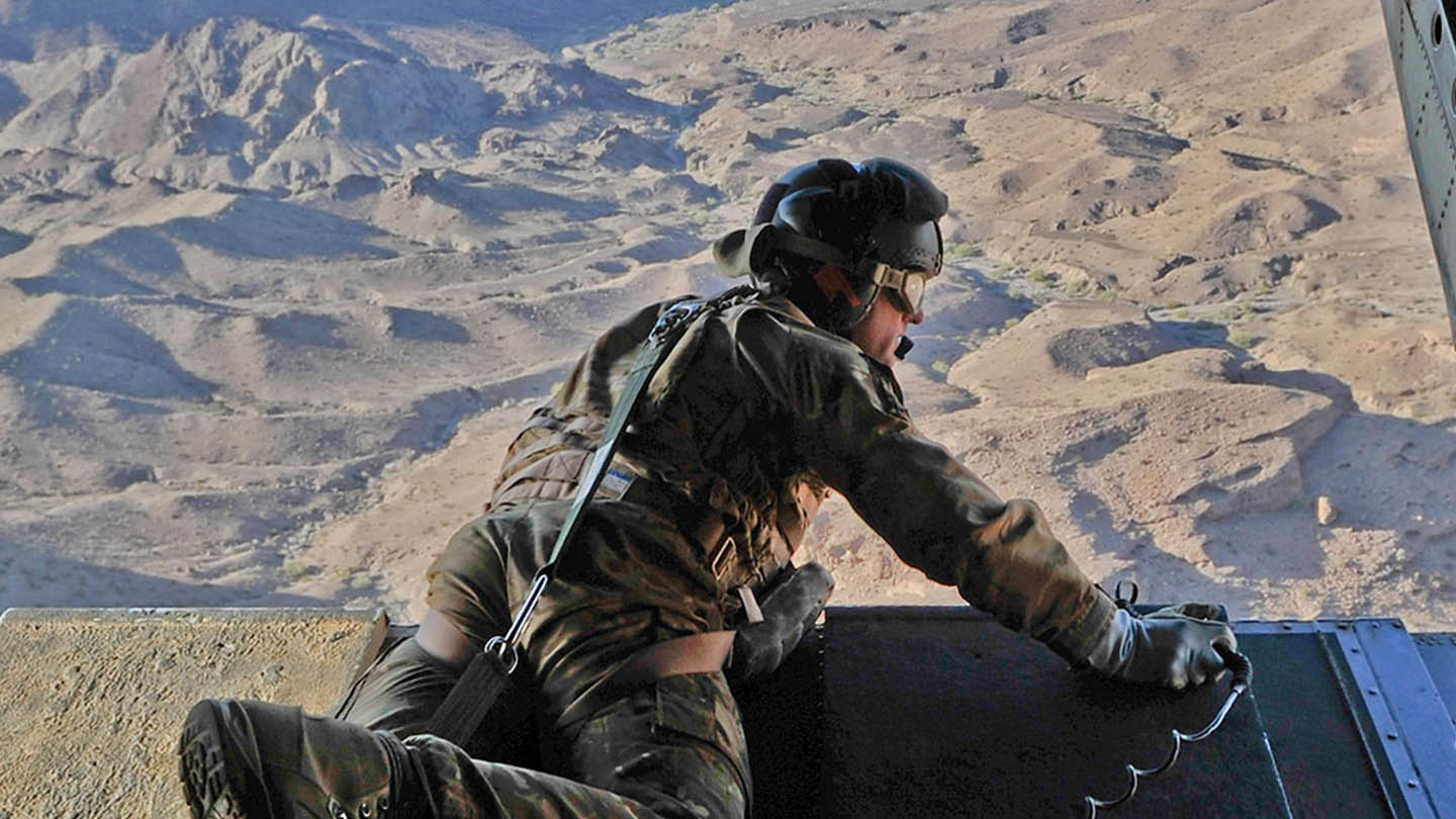 RAF Weapon systems operator leaning over rear ramp of cargo aircraft flying over desert